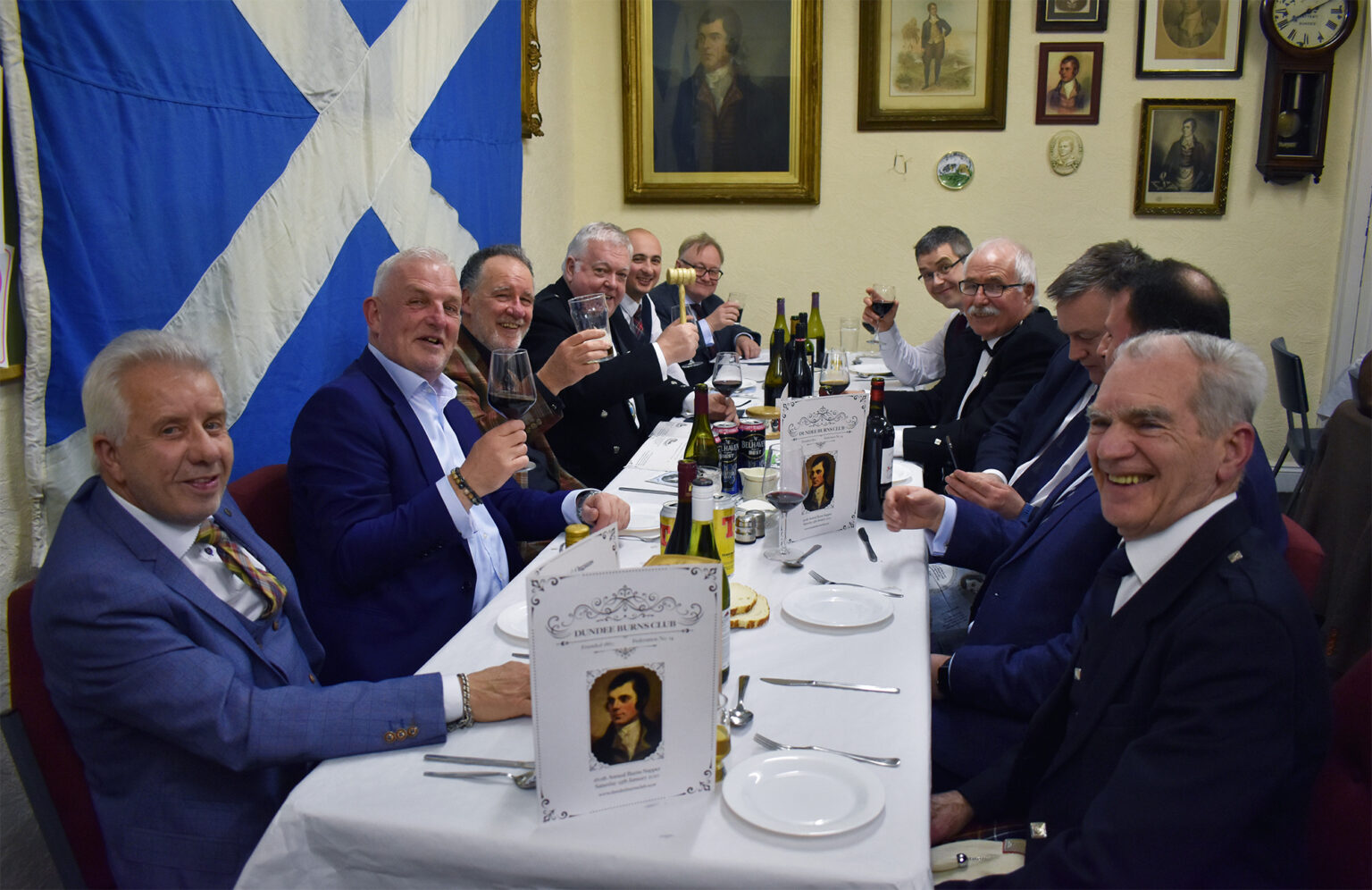 Diners raise their glasses around a long supper table in the club rooms