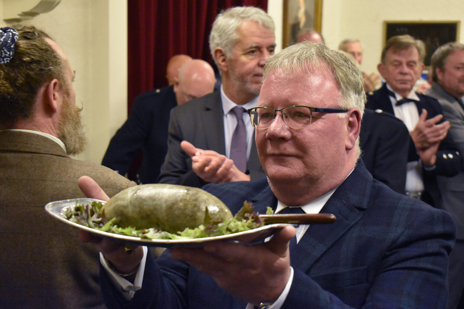 A club member carries in the haggis on a silver platter as diners applaud