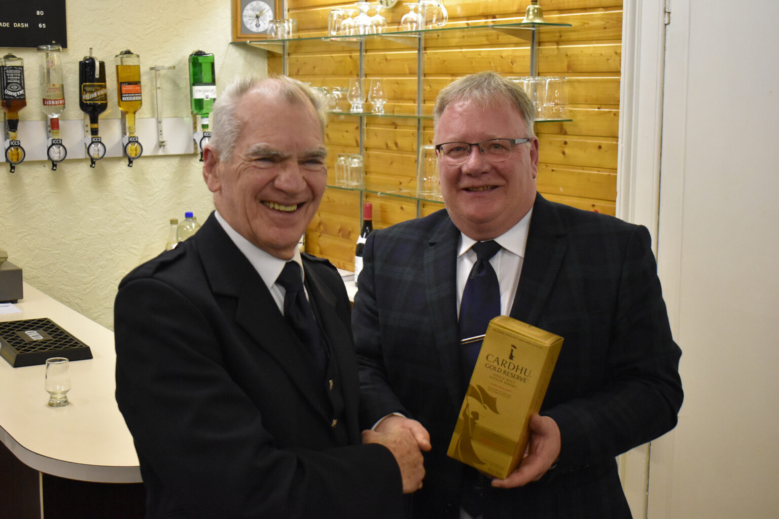 Two men shake hands at the bar as one is presented with a gift