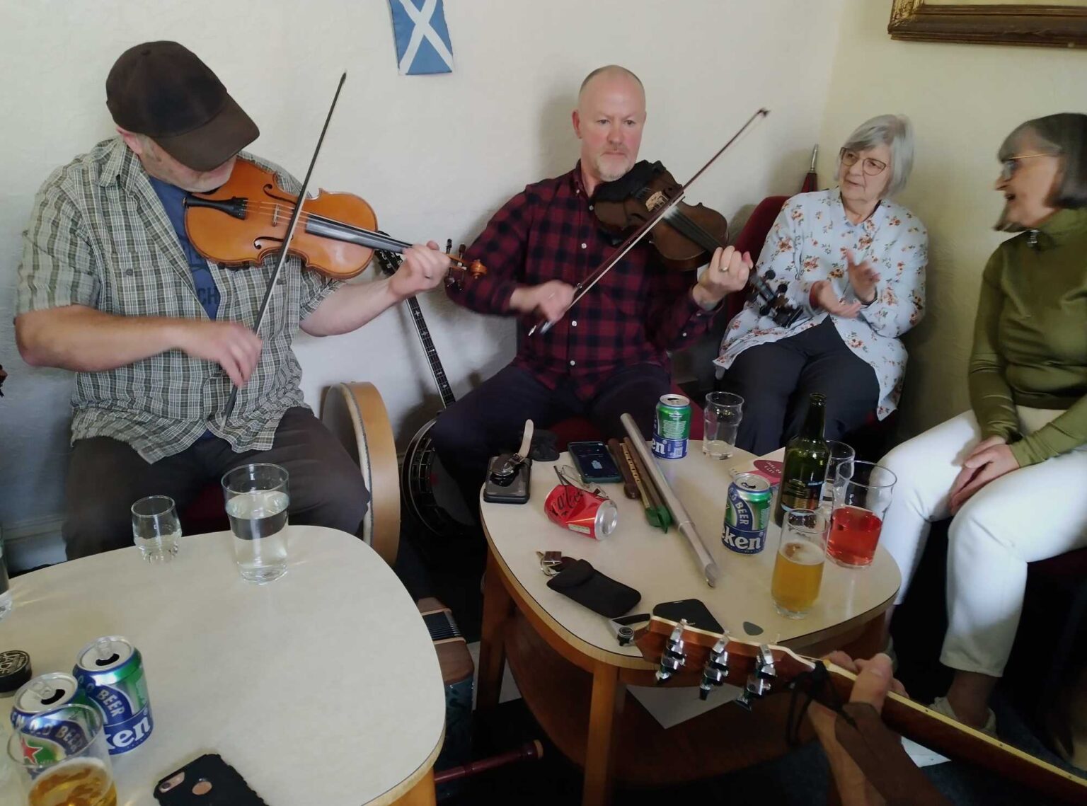 Fiddlers and singers around a small table of drinks during a music session at the club