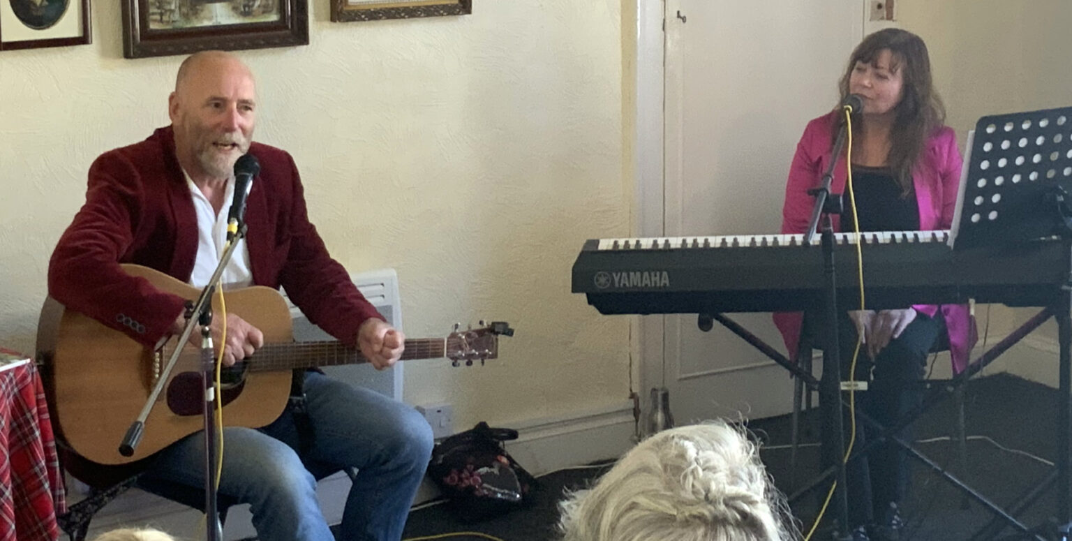 A guitarist and a keyboard player perform in the club room