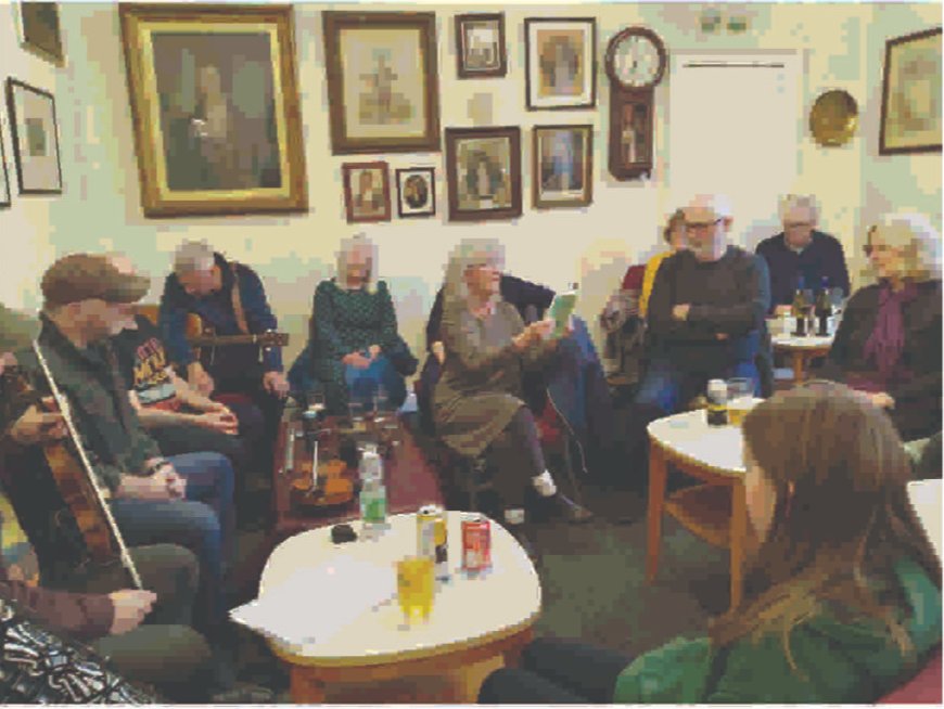An audience in armchairs listening to a reading in the club room