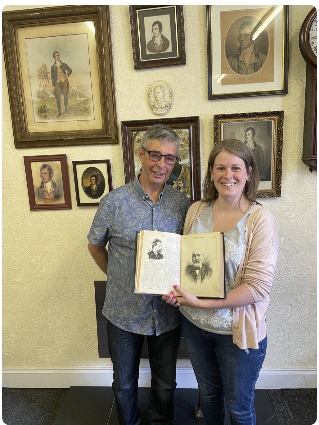 Shona Donaldson holds an open volume showing her great-grandfather David Taylor, in front of portraits of Burns