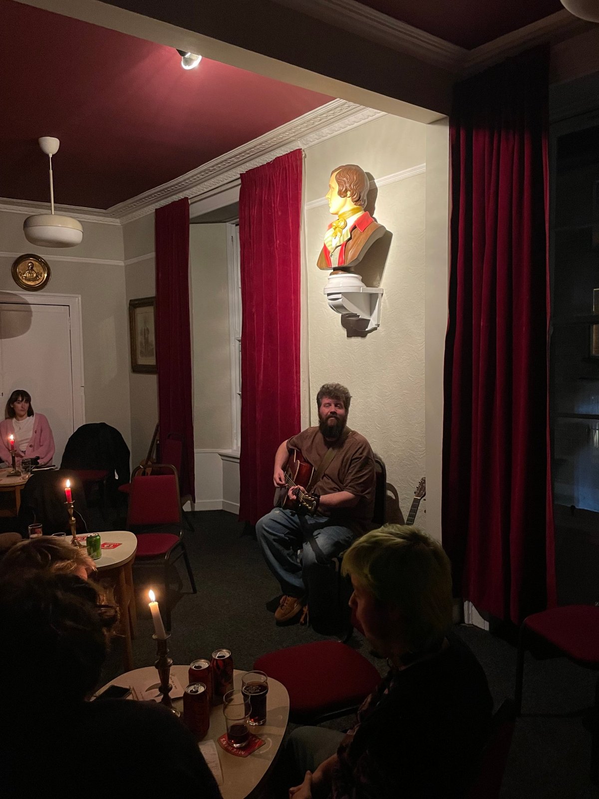 A guitarist plays beneath the painted bust of Burns